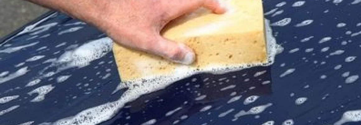 Person wäscht Auto mit Schwamm